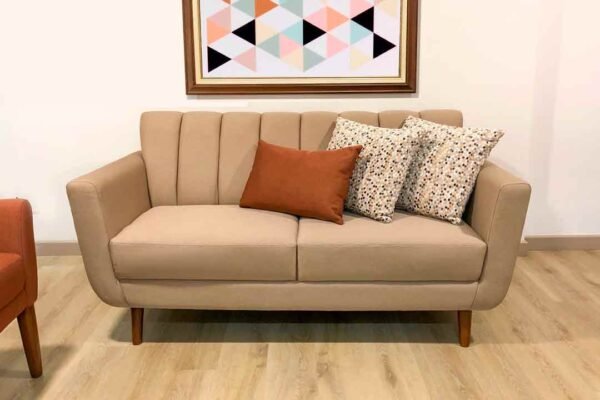Sofá moderno tapizado en tela suave color camel, con cojines decorativos y patas de madera, ideal para una sala pequeña, elegante y con diseño