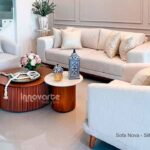 Sala moderna con sofá tapizado en tela beige y dos sillas en el mismo color, decorada con un juego de mesas de centro de madera natural y pintura color almendra con base alistonada