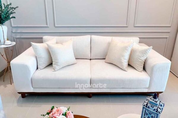 Sofá moderno tapizado en tela suave color beige, con cojines decorativos y patas de madera oscura, ideal para una sala moderna