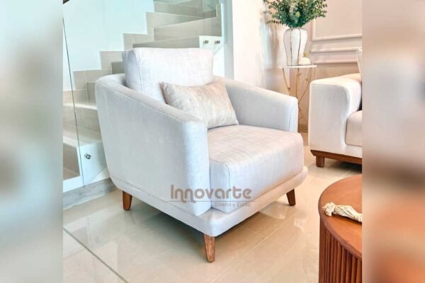 Poltrona tapizada en tela suave, con diseño ergonómico y patas de madera, ideal para salas elegantes