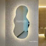 Espejo decorativo con formas orgánicas y luz cálida en su contorno sobre una pared decorada con papel de colgadura en un punto fijo